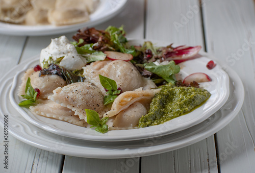 Italian ravioli served with pesto, salad and cream on white plate, wooden backgroud, opy space