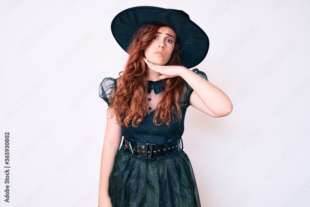 Young beautiful woman wearing witch halloween costume cutting throat with hand as knife, threaten aggression with furious violence Young beautiful woman wearing witch halloween costume cutting throat with hand as knife, threaten aggression with furious violence