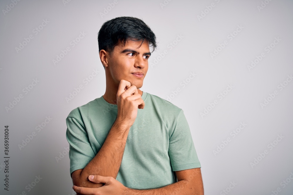 Young handsome man wearing casual t-shirt standing over isolated white background with hand on chin thinking about question, pensive expression. Smiling with thoughtful face. Doubt concept. Young handsome man wearing casual t-shirt standing over isolated white background with hand on chin thinking about question, pensive expression. Smiling with thoughtful face. Doubt concept.