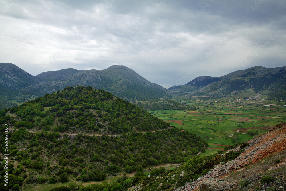 Natural landscape on the island of Crete in Greece, with views of a large green hill, meadows and mountains, in cloudy weather
