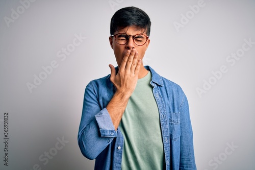 Young handsome man wearing casual shirt and glasses over isolated white background bored yawning tired covering mouth with hand. Restless and sleepiness.