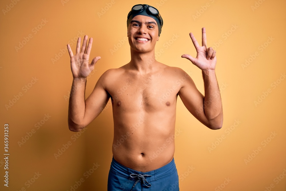 Young handsome man shirtless wearing swimsuit and swim cap over isolated yellow background showing and pointing up with fingers number eight while smiling confident and happy.
