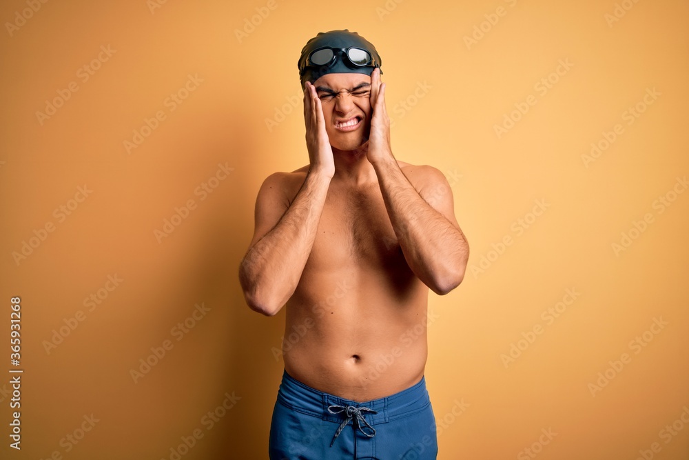 Young handsome man shirtless wearing swimsuit and swim cap over isolated yellow background with hand on headache because stress. Suffering migraine.