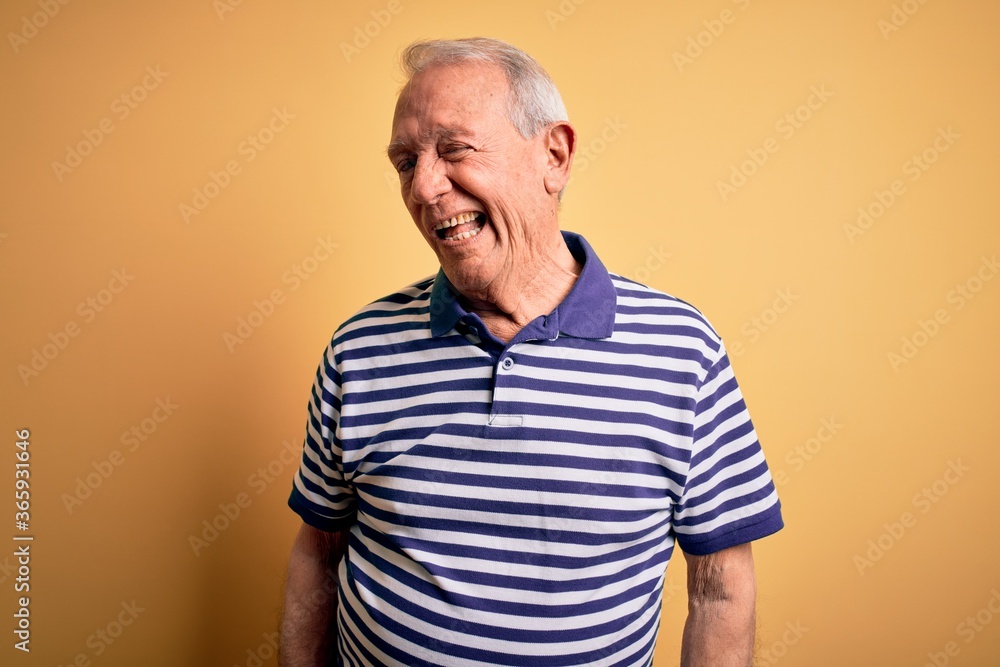 Grey haired senior man wearing casual navy striped t-shirt standing over yellow background winking looking at the camera with sexy expression, cheerful and happy face. Grey haired senior man wearing casual navy striped t-shirt standing over yellow background winking looking at the camera with sexy expression, cheerful and happy face.
