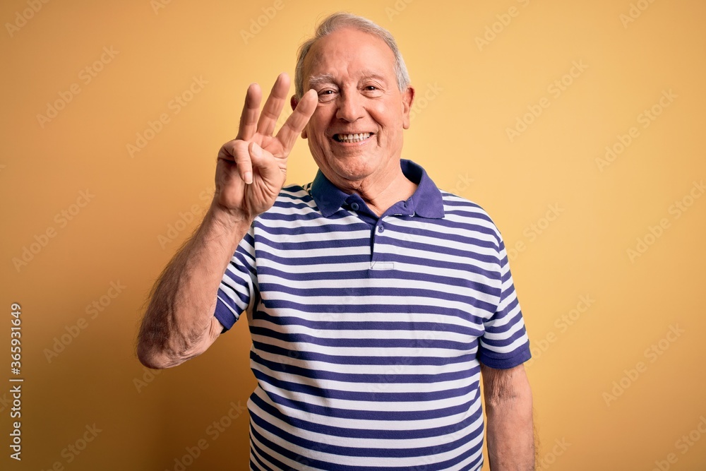 Grey haired senior man wearing casual navy striped t-shirt standing over yellow background showing and pointing up with fingers number three while smiling confident and happy. Grey haired senior man wearing casual navy striped t-shirt standing over yellow background showing and pointing up with fingers number three while smiling confident and happy.