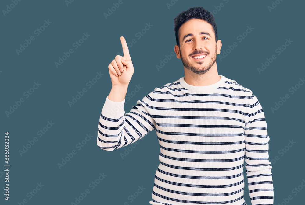 Young hispanic man wearing casual clothes pointing finger up with successful idea. exited and happy. number one. Young hispanic man wearing casual clothes pointing finger up with successful idea. exited and happy. number one.