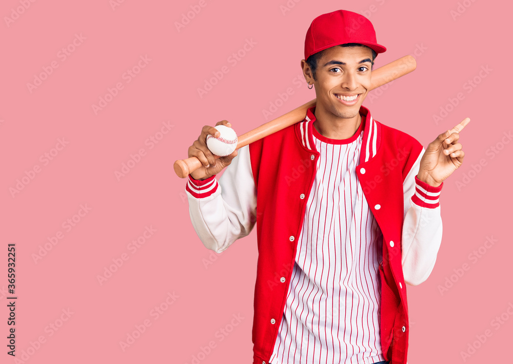 Young african amercian man playing baseball holding bat and ball smiling happy pointing with hand and finger to the side Young african amercian man playing baseball holding bat and ball smiling happy pointing with hand and finger to the side