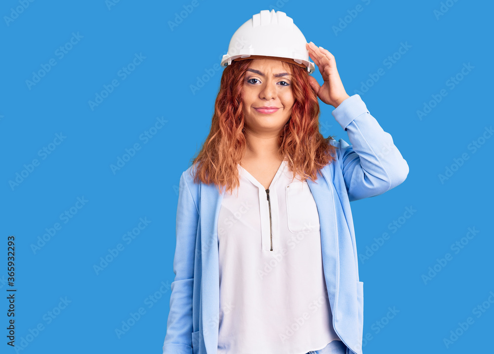 Young latin woman wearing architect hardhat confuse and wonder about question. uncertain with doubt, thinking with hand on head. pensive concept.