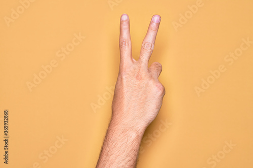 Hand of caucasian young man showing fingers over isolated yellow background counting number 2 showing two fingers  gesturing victory and winner symbol