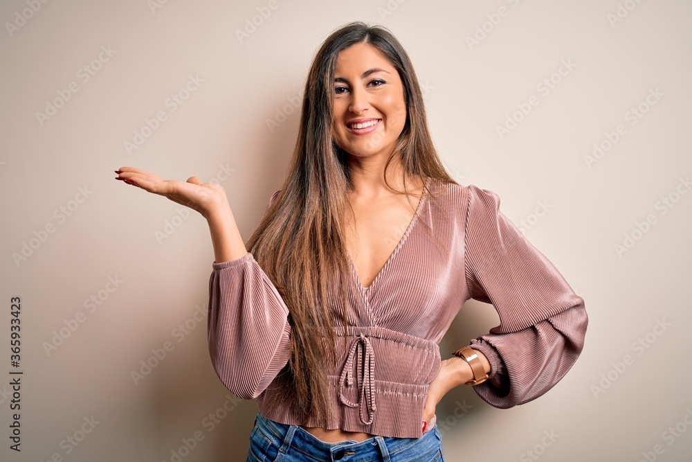 Young beautiful brunette elegant woman with long hair standing over isolated background smiling cheerful presenting and pointing with palm of hand looking at the camera. Young beautiful brunette elegant woman with long hair standing over isolated background smiling cheerful presenting and pointing with palm of hand looking at the camera.