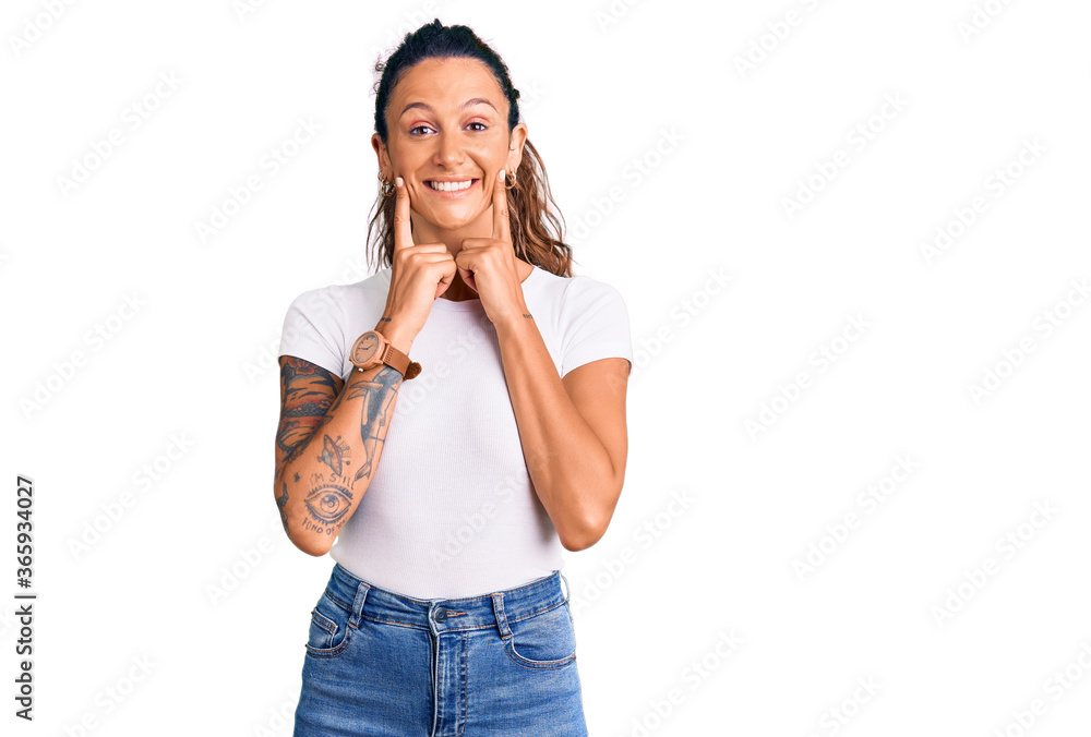 Young hispanic woman with tattoo wearing casual white tshirt smiling with open mouth, fingers pointing and forcing cheerful smile Young hispanic woman with tattoo wearing casual white tshirt smiling with open mouth, fingers pointing and forcing cheerful smile