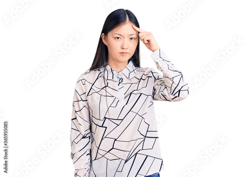 Young beautiful chinese woman wearing casual shirt pointing unhappy to pimple on forehead, ugly infection of blackhead. acne and skin problem photo