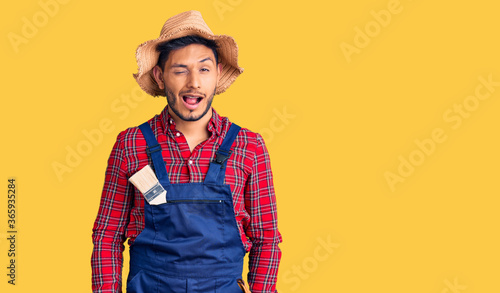 Handsome latin american young man weaing handyman uniform winking looking at the camera with sexy expression, cheerful and happy face.