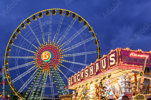 Night scenery atmosphere of colourful illuminated " GLUCKSHAUS " medieval gambling stall and background of Bellevue Ferris wheel, Rheinkirmes funfair festival.