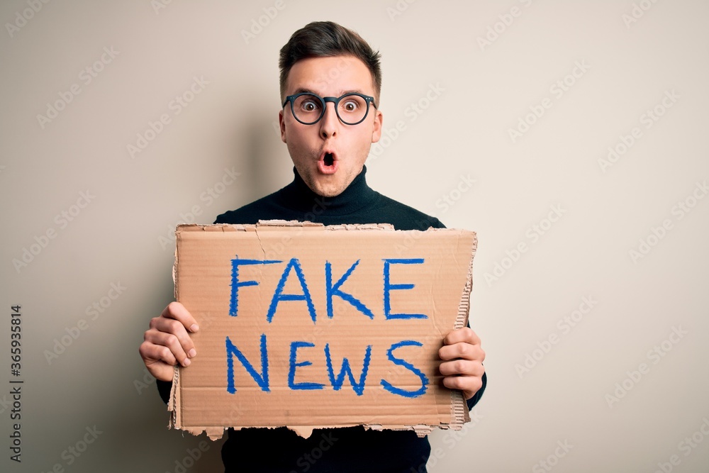Young handsome caucasian man holding protest carboard for desinformation and fake news scared in shock with a surprise face, afraid and excited with fear expression Young handsome caucasian man holding protest carboard for desinformation and fake news scared in shock with a surprise face, afraid and excited with fear expression