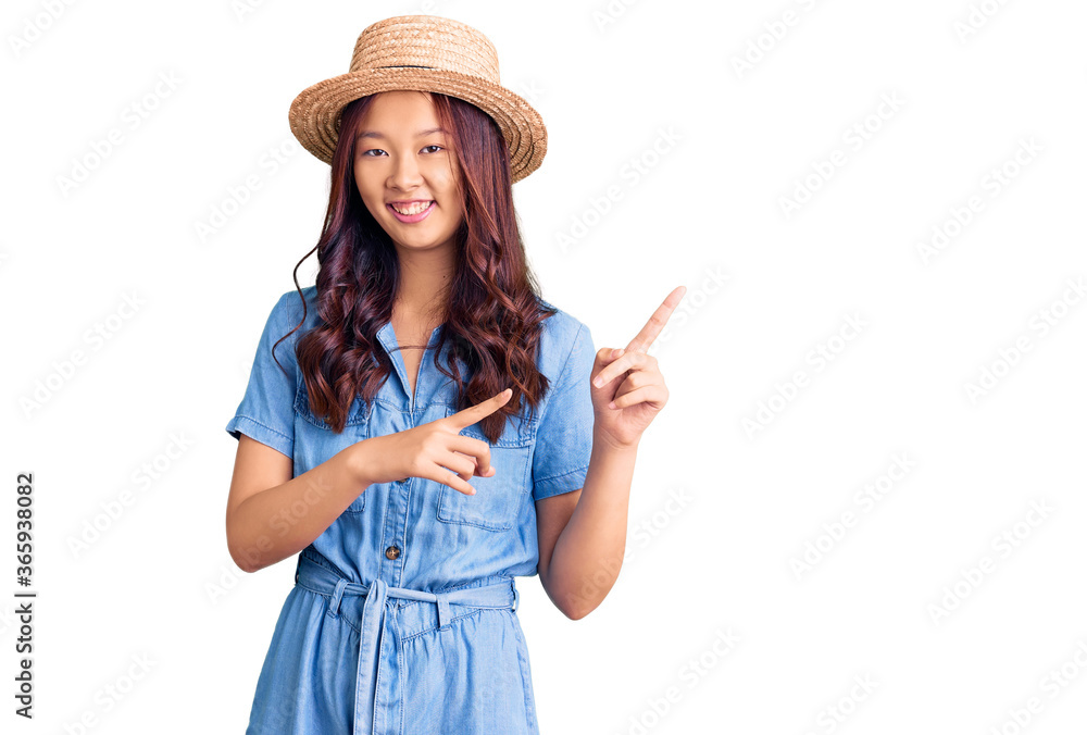 Young beautiful chinese girl wearing summer hat smiling and looking at the camera pointing with two hands and fingers to the side. Young beautiful chinese girl wearing summer hat smiling and looking at the camera pointing with two hands and fingers to the side.