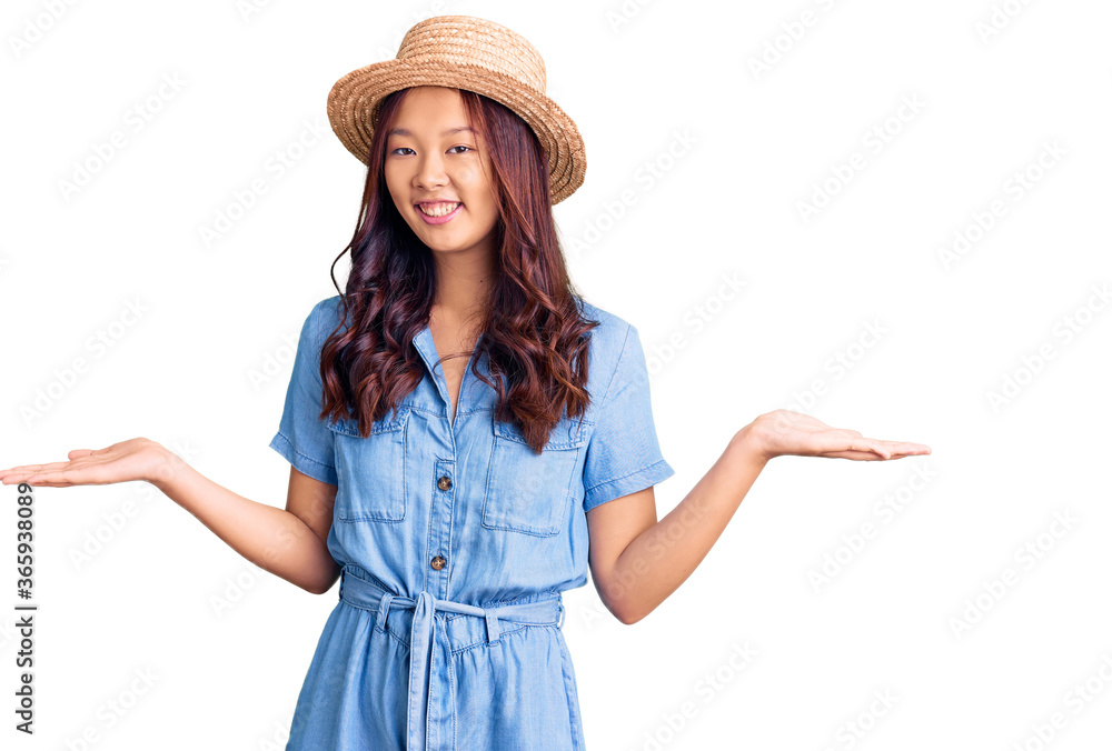 Young beautiful chinese girl wearing summer hat smiling showing both hands open palms, presenting and advertising comparison and balance Young beautiful chinese girl wearing summer hat smiling showing both hands open palms, presenting and advertising comparison and balance