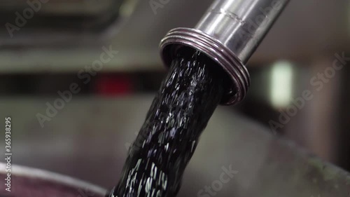 red wine flows out from tap of tank inside a wine cellar prodution slow motion photo