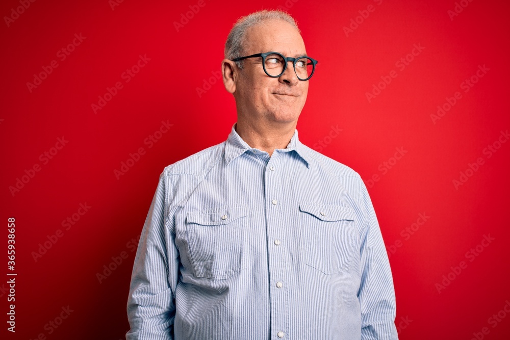 Middle age handsome hoary man wearing casual striped shirt and glasses over red background smiling looking to the side and staring away thinking. Middle age handsome hoary man wearing casual striped shirt and glasses over red background smiling looking to the side and staring away thinking.