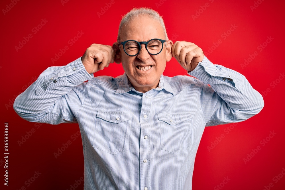 Middle age handsome hoary man wearing casual striped shirt and glasses over red background Smiling pulling ears with fingers, funny gesture. Audition problem Middle age handsome hoary man wearing casual striped shirt and glasses over red background Smiling pulling ears with fingers, funny gesture. Audition problem