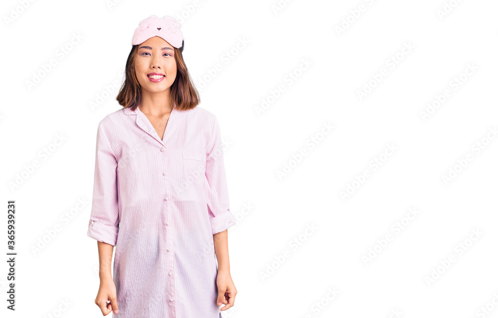 Young beautiful chinese girl wearing sleep mask and pajama with a happy and cool smile on face. lucky person. Young beautiful chinese girl wearing sleep mask and pajama with a happy and cool smile on face. lucky person.
