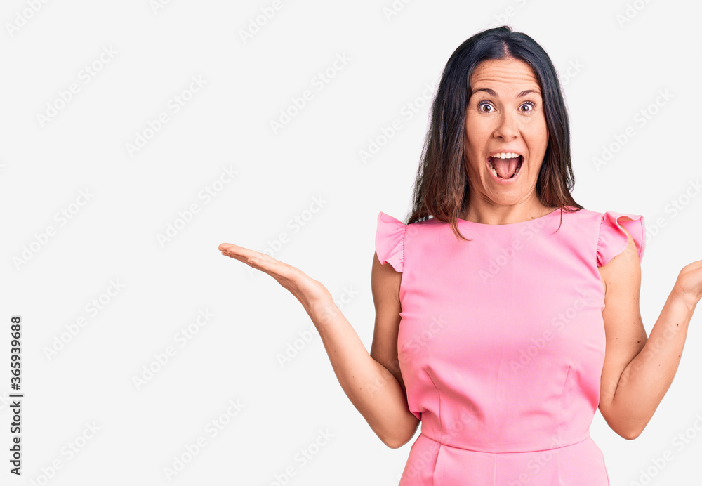 Young beautiful brunette woman wearing casual dress celebrating victory with happy smile and winner expression with raised hands