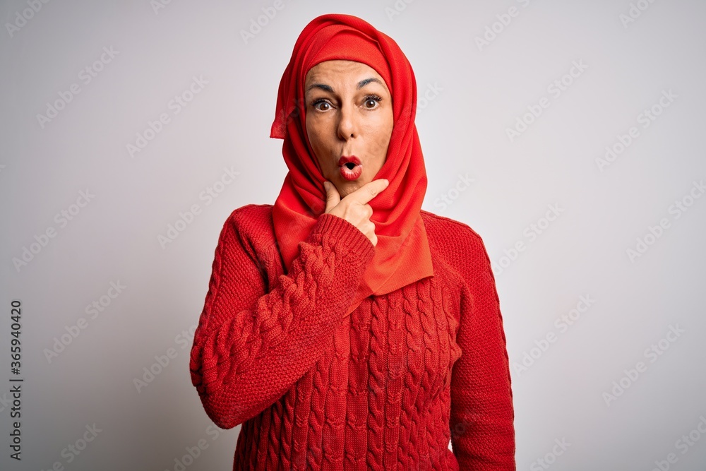 Middle age brunette woman wearing muslim traditional hijab over isolated white background Looking fascinated with disbelief, surprise and amazed expression with hands on chin Middle age brunette woman wearing muslim traditional hijab over isolated white background Looking fascinated with disbelief, surprise and amazed expression with hands on chin