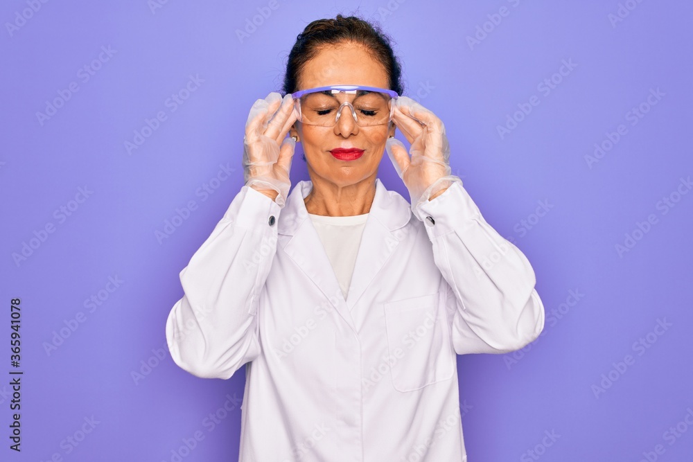 Middle age senior scientist woman wearing coat and laboratory glasses over purple background suffering from headache desperate and stressed because pain and migraine. Hands on head. Middle age senior scientist woman wearing coat and laboratory glasses over purple background suffering from headache desperate and stressed because pain and migraine. Hands on head.