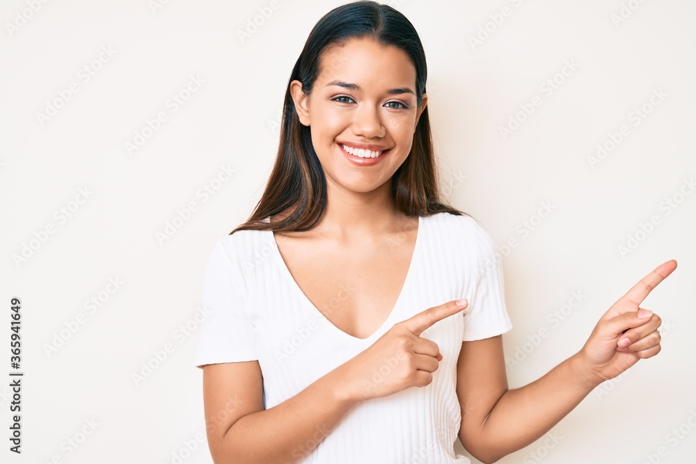 Young beautiful latin girl wearing casual white tshirt smiling and looking at the camera pointing with two hands and fingers to the side. Young beautiful latin girl wearing casual white tshirt smiling and looking at the camera pointing with two hands and fingers to the side.