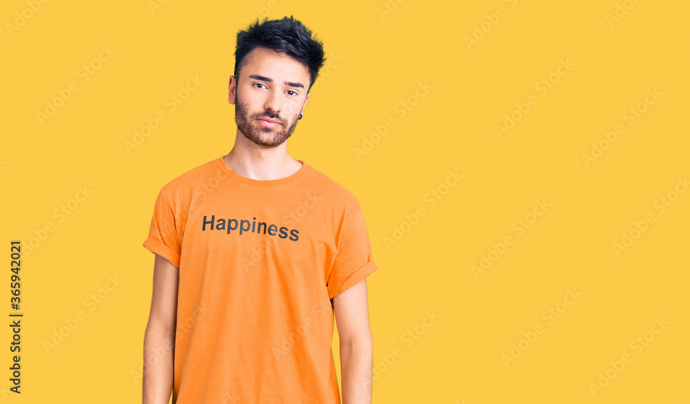 Young hispanic man wearing t shirt with happiness word message relaxed with serious expression on face. simple and natural looking at the camera. Young hispanic man wearing t shirt with happiness word message relaxed with serious expression on face. simple and natural looking at the camera.