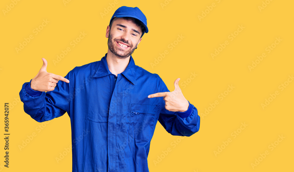 Young hispanic man wearing painter uniform looking confident with smile on face, pointing oneself with fingers proud and happy.