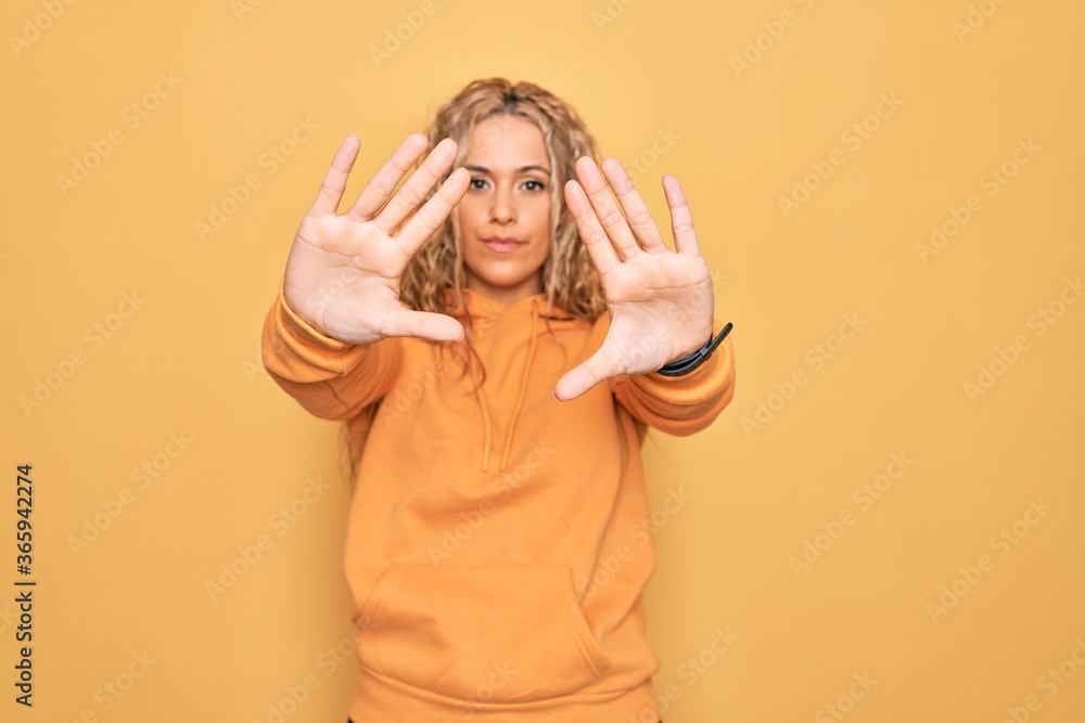 Young beautiful blonde sporty woman wearing casual sweatshirt over yellow background doing frame using hands palms and fingers, camera perspective Young beautiful blonde sporty woman wearing casual sweatshirt over yellow background doing frame using hands palms and fingers, camera perspective