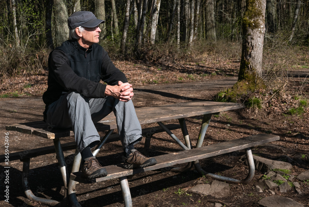 Single senior man sitting atop a picnic table in the woods contemplating Single senior man sitting atop a picnic table in the woods contemplating