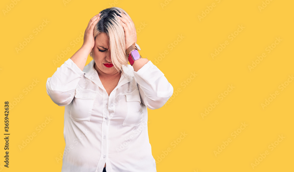 Young blonde plus size woman wearing casual shirt suffering from headache desperate and stressed because pain and migraine. hands on head. Young blonde plus size woman wearing casual shirt suffering from headache desperate and stressed because pain and migraine. hands on head.