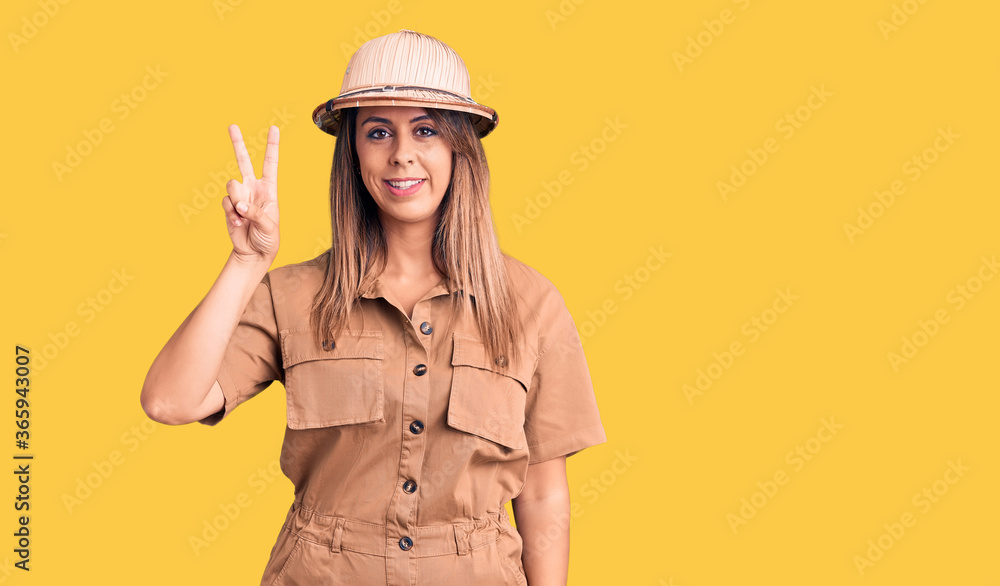 Young beautiful woman wearing explorer hat smiling with happy face winking at the camera doing victory sign. number two. Young beautiful woman wearing explorer hat smiling with happy face winking at the camera doing victory sign. number two.
