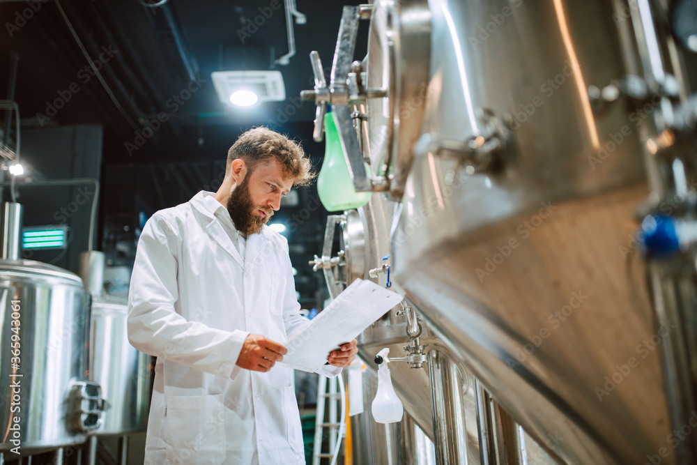 Caucasian male professional technologist expert in white suit operating production machine in food factory and doing quality control and holding checklist. Checking production in food industry. Caucasian male professional technologist expert in white suit operating production machine in food factory and doing quality control and holding checklist. Checking production in food industry.