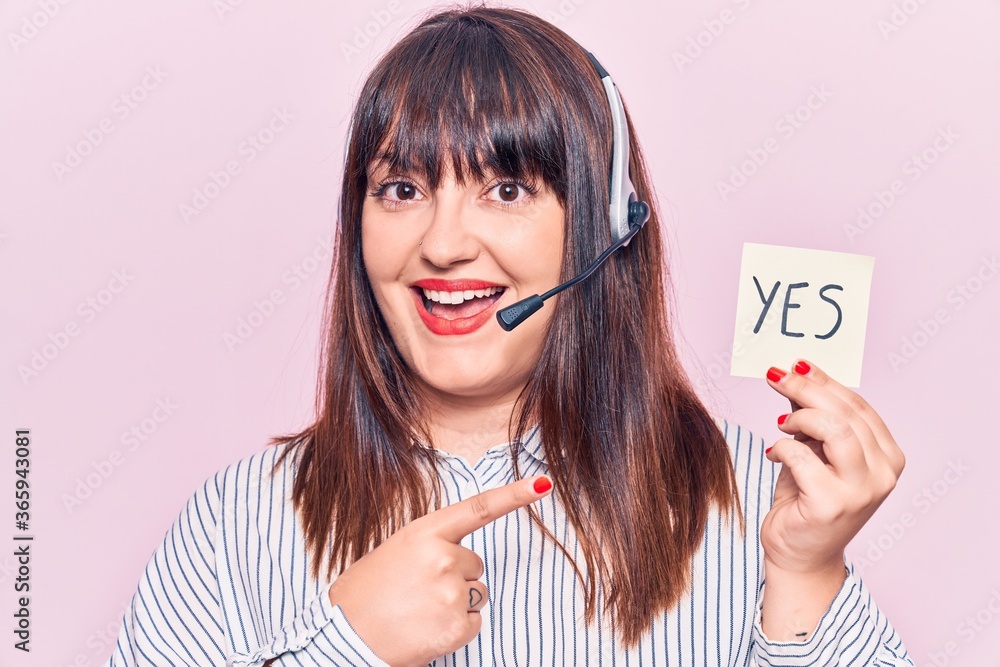 Young plus size woman wearing call center agent headset holding yes reminder smiling happy pointing with hand and finger Young plus size woman wearing call center agent headset holding yes reminder smiling happy pointing with hand and finger