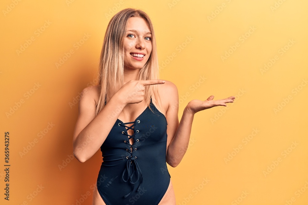 Young beautiful blonde girl wearing swimwear amazed and smiling to the camera while presenting with hand and pointing with finger. Young beautiful blonde girl wearing swimwear amazed and smiling to the camera while presenting with hand and pointing with finger.