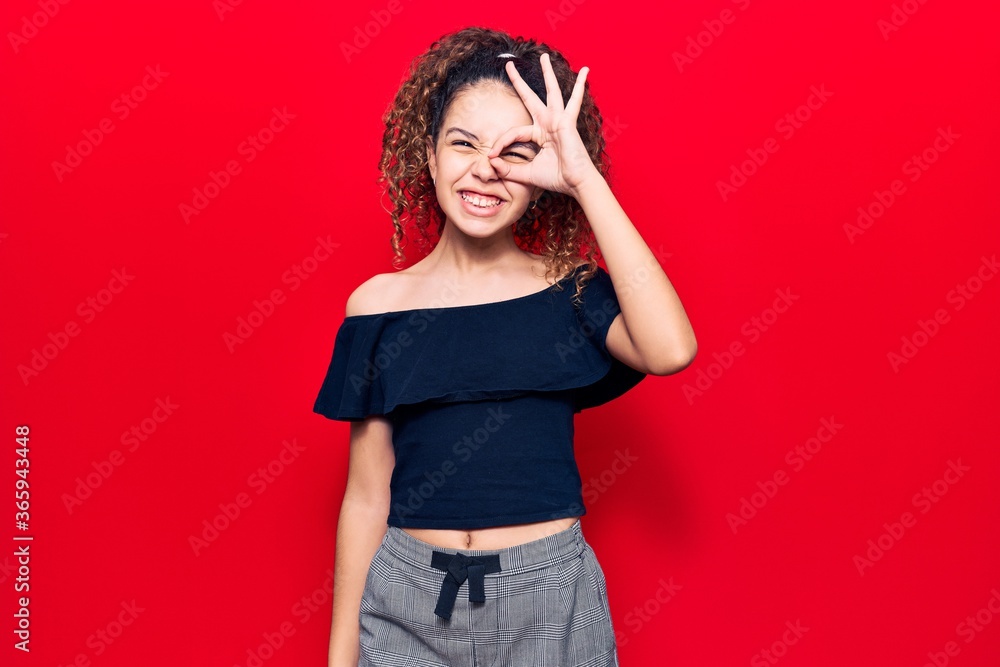 Beautiful kid girl with curly hair wearing casual clothes smiling happy doing ok sign with hand on eye looking through fingers Beautiful kid girl with curly hair wearing casual clothes smiling happy doing ok sign with hand on eye looking through fingers