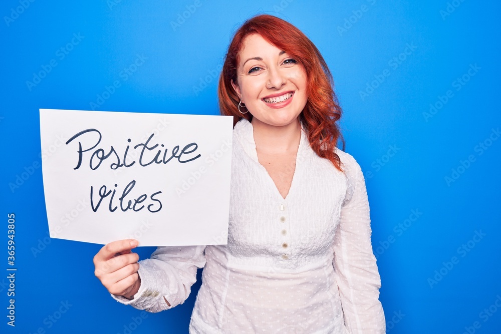 Young redhead woman asking for optimist attitude holding paper with positive vibes message looking positive and happy standing and smiling with a confident smile showing teeth Young redhead woman asking for optimist attitude holding paper with positive vibes message looking positive and happy standing and smiling with a confident smile showing teeth