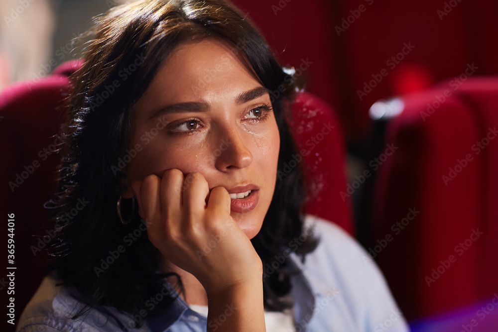Naklejka premium Head and shoulders portrait of young woman crying in cinema while watching sad drama movie, copy space