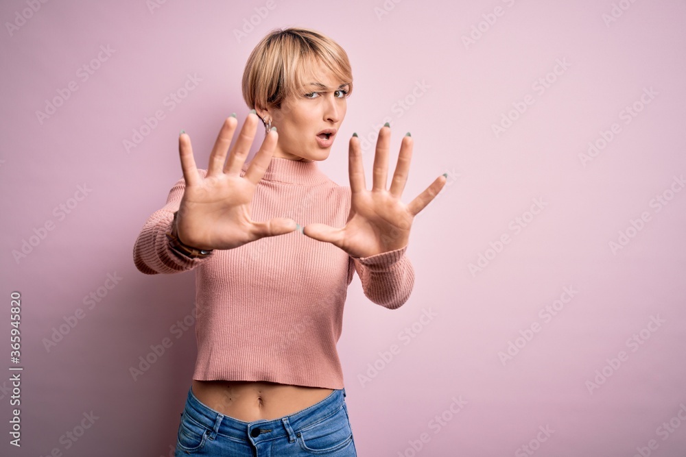 Young blonde woman with short hair wearing casual turtleneck sweater over pink background doing stop gesture with hands palms, angry and frustration expression Young blonde woman with short hair wearing casual turtleneck sweater over pink background doing stop gesture with hands palms, angry and frustration expression