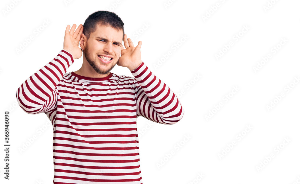 Young handsome man wearing striped sweater trying to hear both hands on ear gesture, curious for gossip. hearing problem, deaf Young handsome man wearing striped sweater trying to hear both hands on ear gesture, curious for gossip. hearing problem, deaf