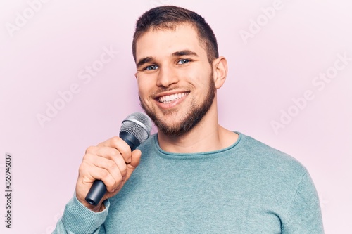 Young handsome man singing song using microphone looking positive and happy standing and smiling with a confident smile showing teeth