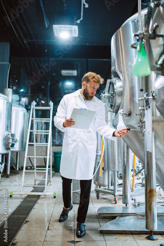 Full lenght of caucasian male professional technologist expert in white suit operating production machine in food factory and doing quality control and holding checklist. 