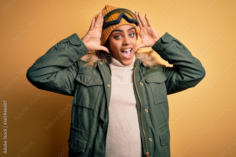 Young african american afro skier girl wearing snow sportswear and ski goggles Smiling cheerful playing peek a boo with hands showing face. Surprised and exited Young african american afro skier girl wearing snow sportswear and ski goggles Smiling cheerful playing peek a boo with hands showing face. Surprised and exited