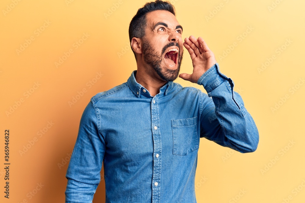 Young hispanic man wearing casual clothes shouting and screaming loud to side with hand on mouth. communication concept. Young hispanic man wearing casual clothes shouting and screaming loud to side with hand on mouth. communication concept.