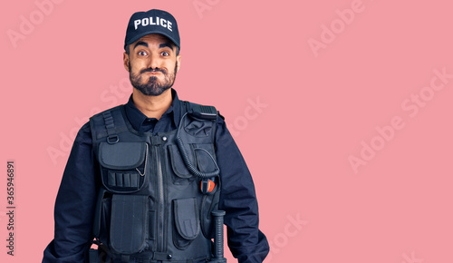 Young hispanic man wearing police uniform puffing cheeks with funny face. mouth inflated with air, crazy expression.