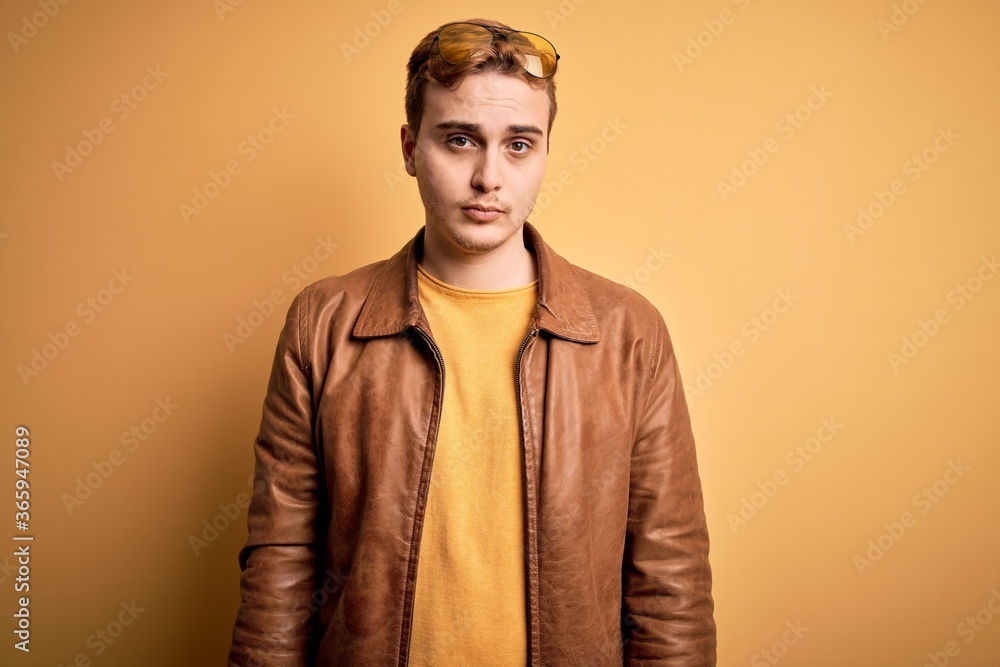 Young handsome redhead man wearing casual leather jacket over isolated yellow background Relaxed with serious expression on face. Simple and natural looking at the camera. Young handsome redhead man wearing casual leather jacket over isolated yellow background Relaxed with serious expression on face. Simple and natural looking at the camera.