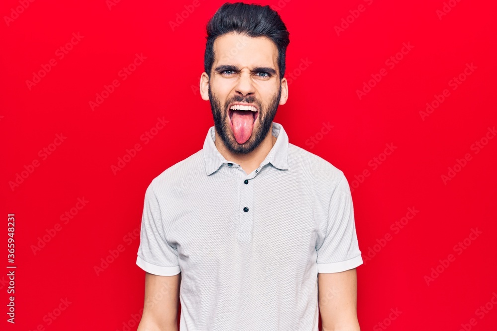 Fototapeta premium Young handsome man with beard wearing casual polo sticking tongue out happy with funny expression. emotion concept.